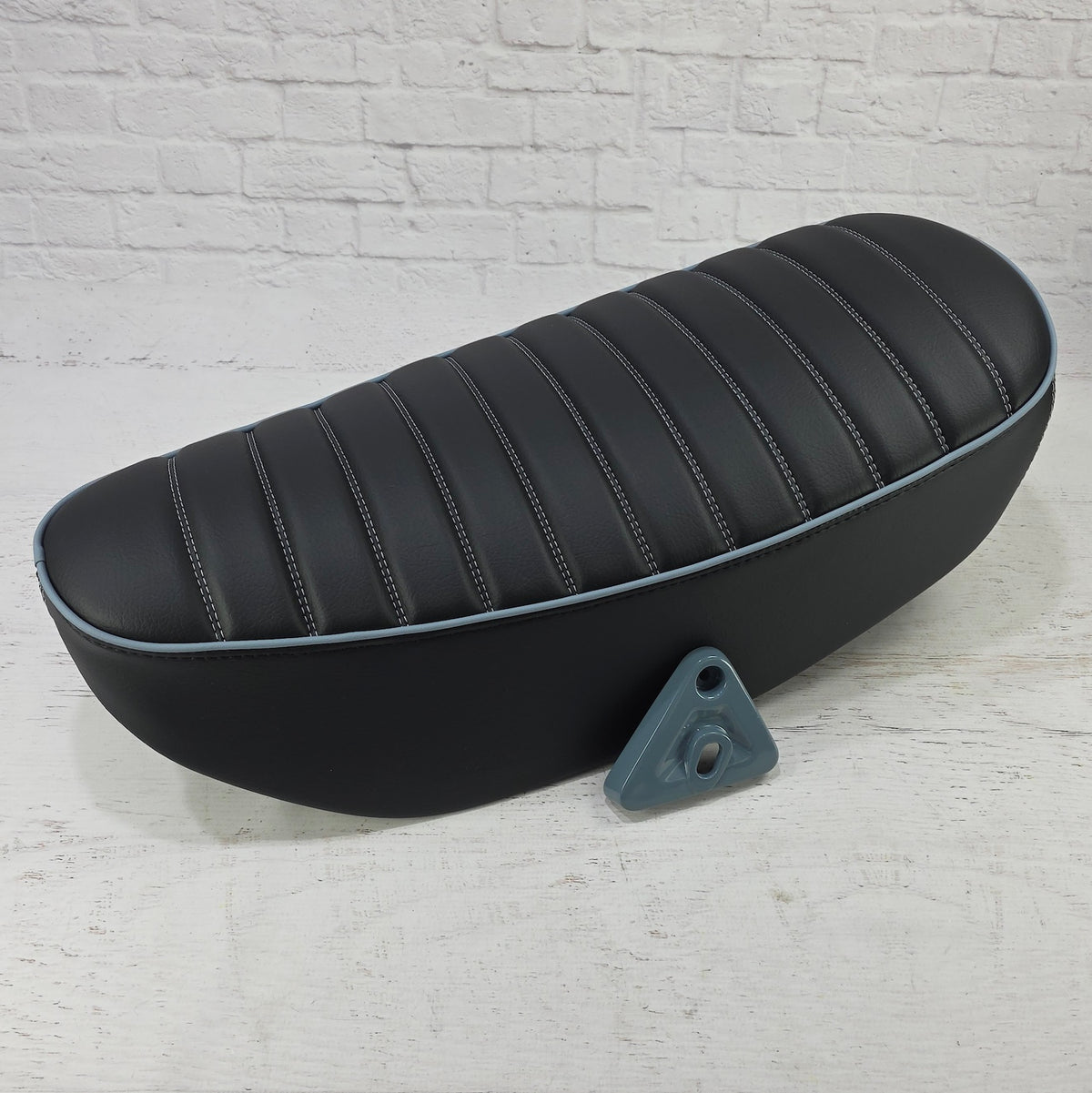 Black tuck-and-roll Honda DAX 125 seat cover with Pearl Gray stitching and piping with Honda mounting bracket as a color match swatch, handmade by Cheeky Seats
