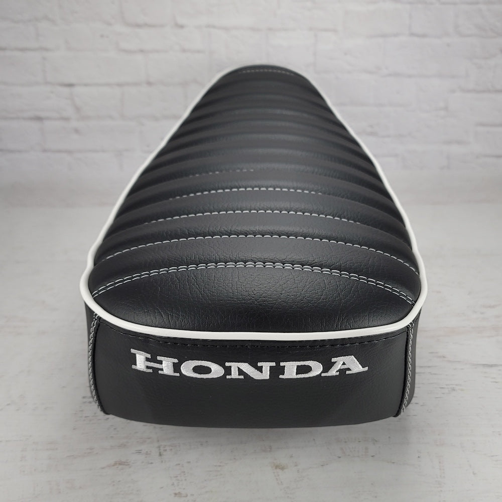 Rear view of a black tuck-and-roll Honda DAX 125 seat cover with white piping and embroidered Honda logo, handmade by Cheeky Seats