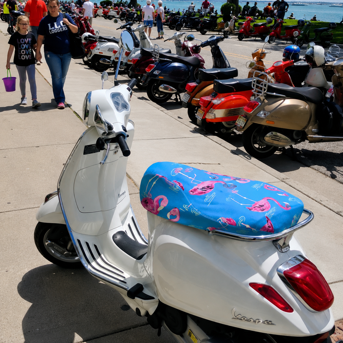 Pink Flamingos seat cover fitted to a white Vespa at a waterfront scooter gathering, handmade by Cheeky Seats.