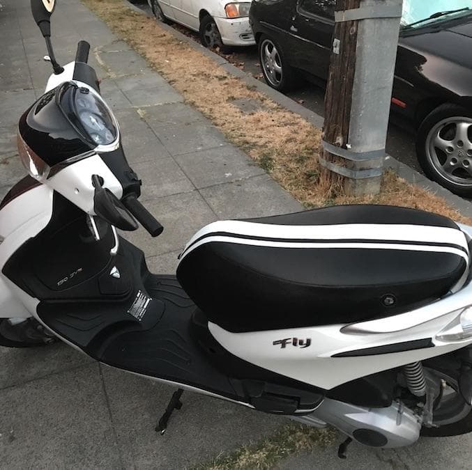 White Piaggio Fly scooter with a black seat cover and twin white racing stripes, handmade by Cheeky Seats