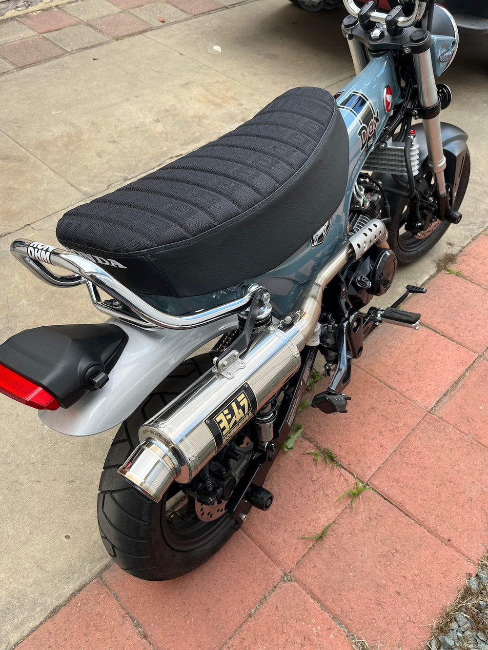 Gray-blue Honda DAX 125 with a black BRIDE tuck-and-roll seat cover, visible DAX and Honda badges, handmade by Cheeky Seats