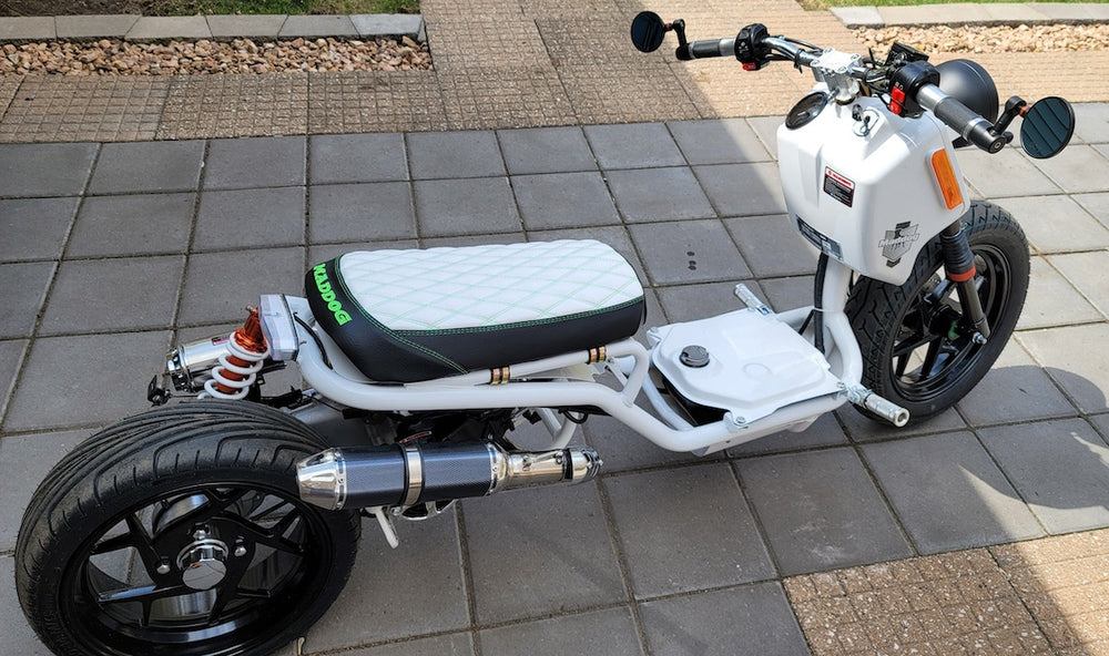 White Maddog scooter in a driveway with a white diamond seat cover featuring green accent stitching, handmade by Cheeky Seats.