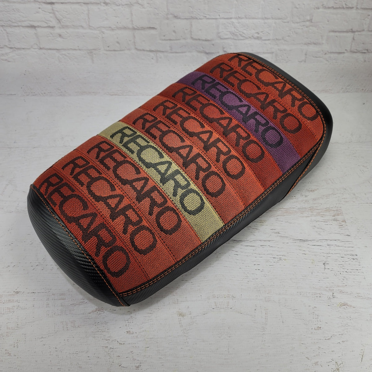 Recaro Sunrise fabric seat cover with multicolor RECARO text pattern in orange, red, purple, and yellow stripes, orange stitching, and dark side panels, handmade by Cheeky Seats