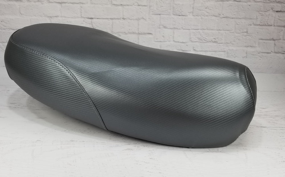 Low side view of a gray carbon-fiber-textured Yamaha Zuma II BWS 49/50 Prebug seat cover, handmade by Cheeky Seats