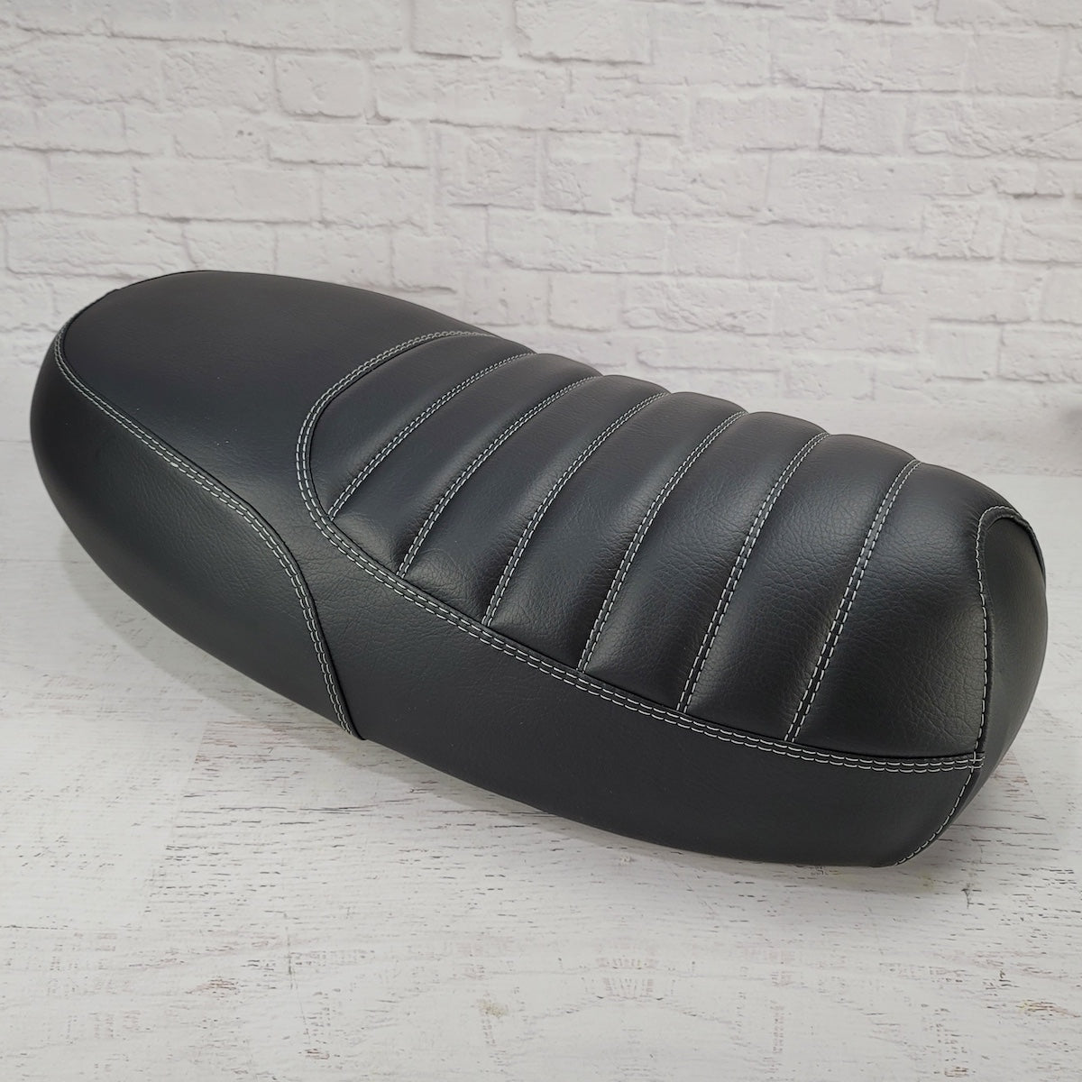 Front three-quarter view of a black Yamaha Zuma II BWS 49/50 Prebug tuck-and-roll seat cover with contrasting gray double stitching, handmade by Cheeky Seats