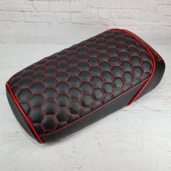 Black hexagon honeycomb-stitched Maddog seat cover with red stitching and red piping, three-quarter view against a white brick backdrop, handmade by Cheeky Seats