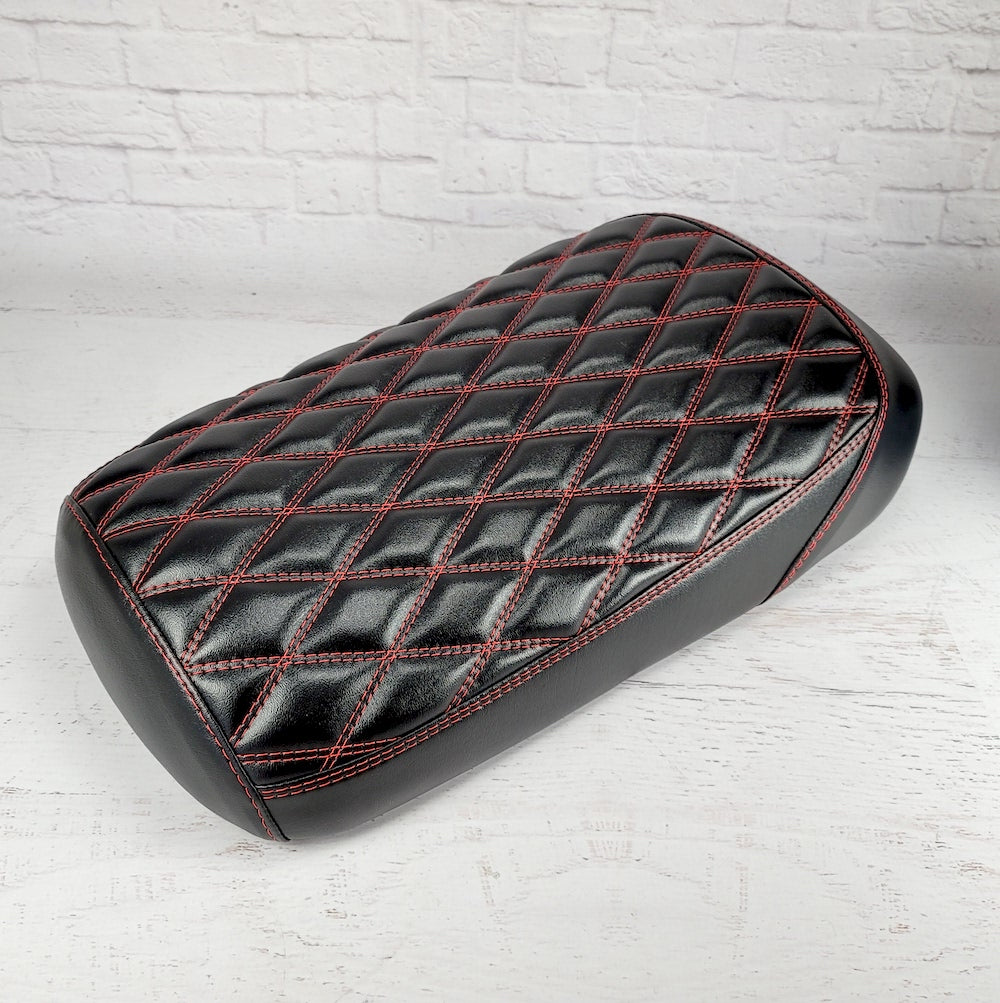 Satin black diamond-stitched Maddog seat cover with red contrast stitching and a glossy wet-look sheen, three-quarter overhead view, handmade by Cheeky Seats