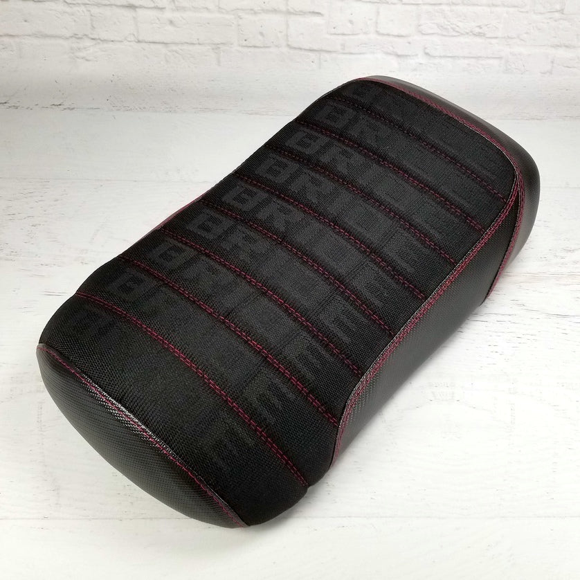 Front three-quarter view of the black Bride fabric Maddog seat cover with black carbon fiber sides, red stitching, handmade by Cheeky Seats